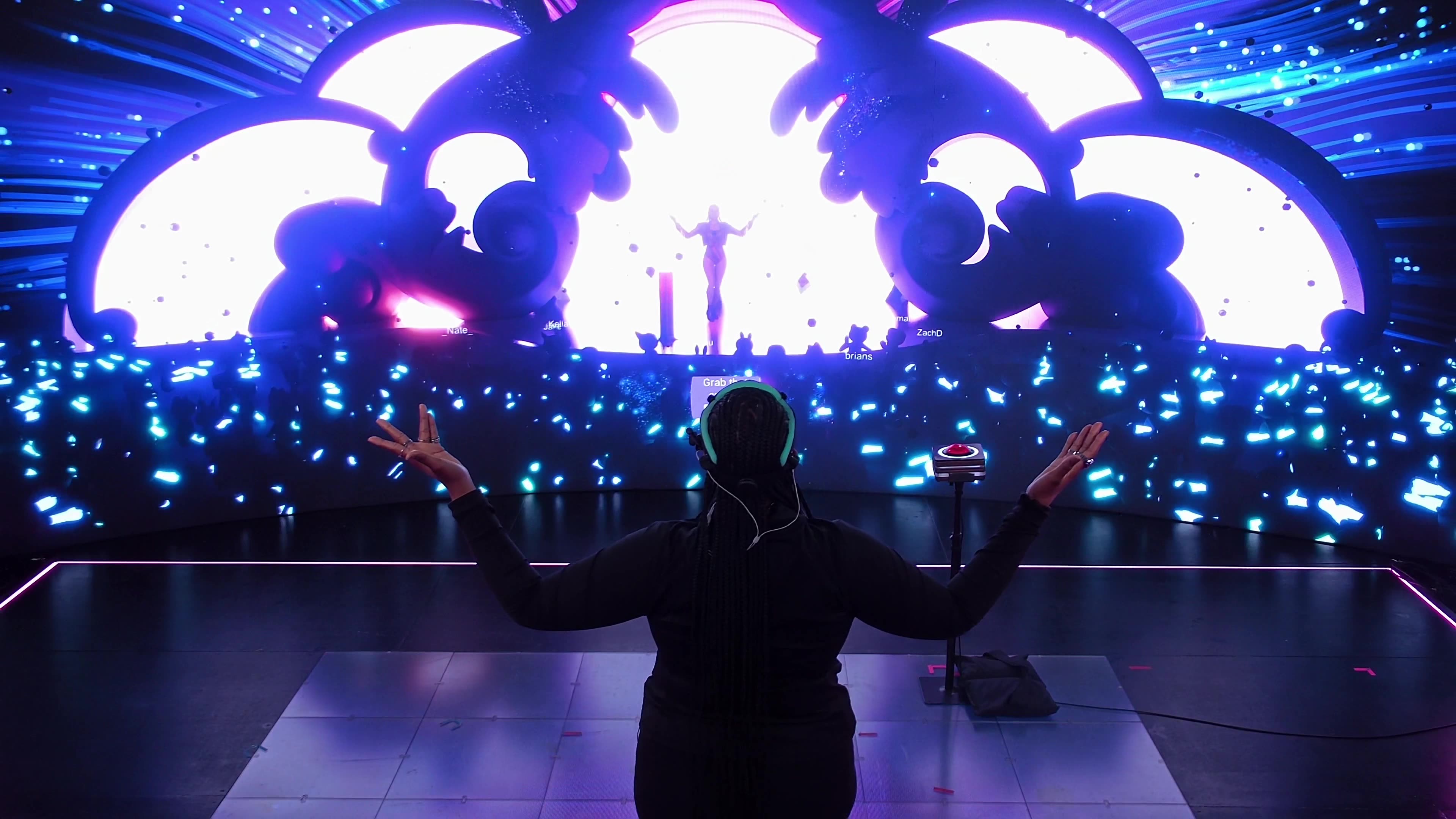 Audience perspective with silhouetted avatar watching massive cloud-shaped stage structures